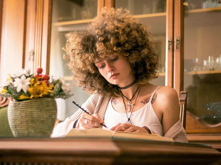 Woman with curly hair writing thoughtfully in an open journal
